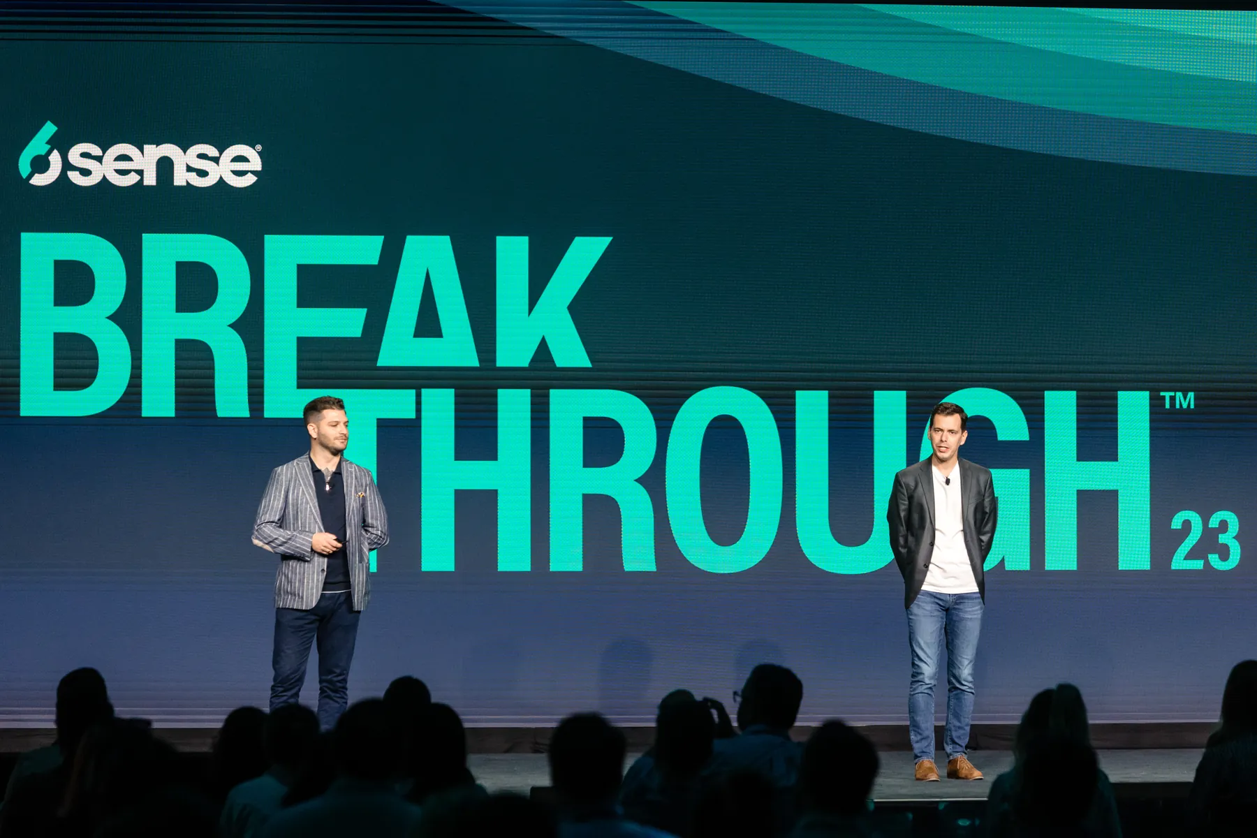 Two presenters on stage in front of the 6sense Breakthrough 23 backdrop, with the audience in the foreground